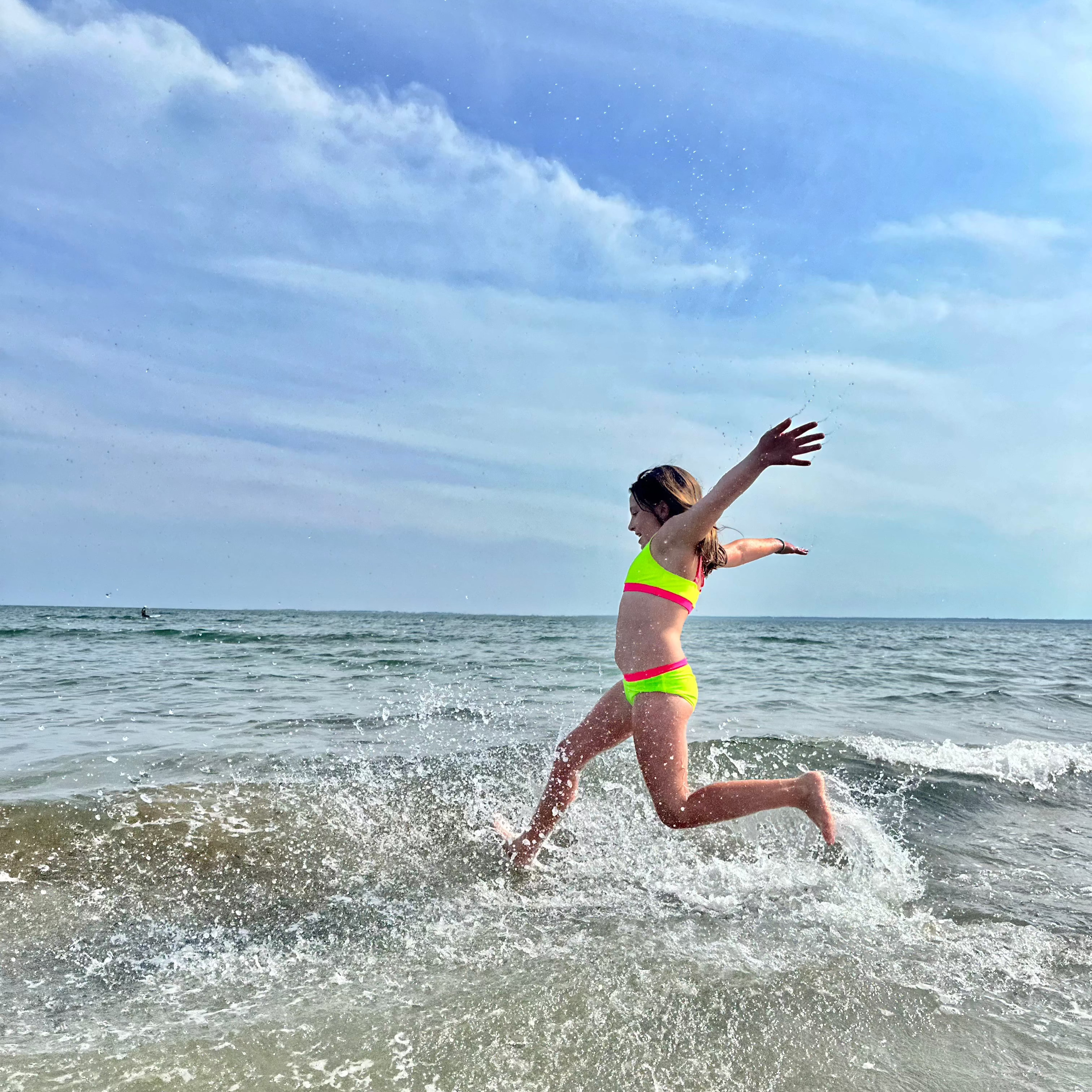 Tween girl jumping waves wearing a neon yellow and neon hot pink bikini from the bright swimwear line from HiViz.